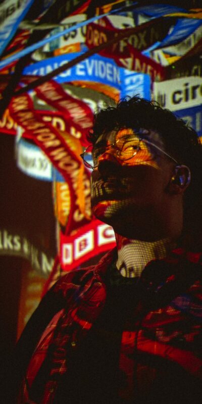 A man stands illuminated by colorful projections, creating a modern artistic scene.