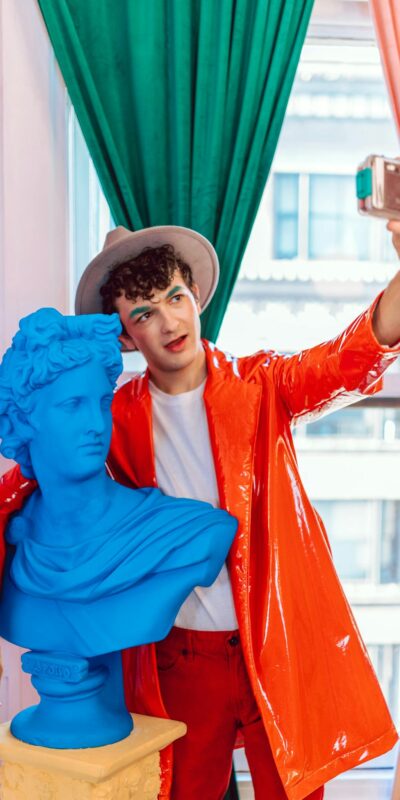 Colorful portrait of a man taking a selfie with a blue statue indoors.